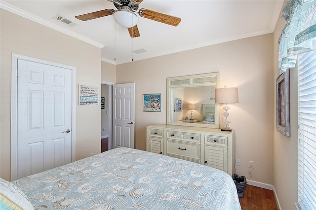 bedroom featuring a ceiling fan, baseboards, wood finished floors, visible vents, and ornamental molding