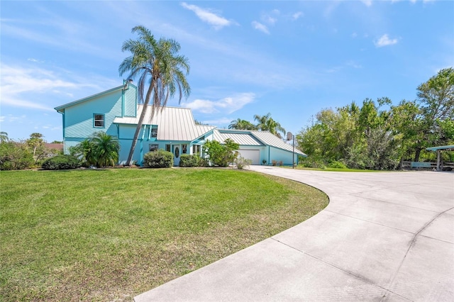 view of front of home featuring a front yard, a standing seam roof, concrete driveway, a garage, and metal roof