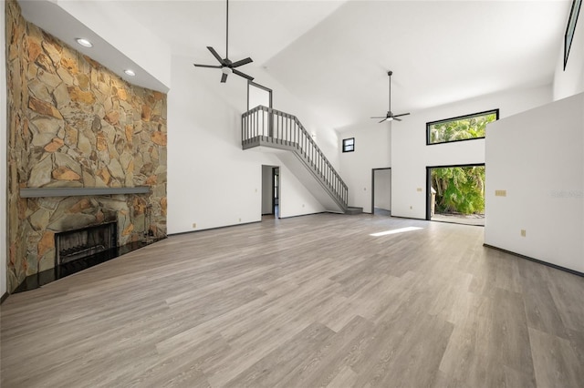 unfurnished living room with a fireplace, stairs, a ceiling fan, and wood finished floors