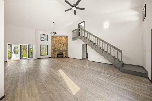 unfurnished living room featuring a ceiling fan, wood finished floors, high vaulted ceiling, a fireplace, and stairs