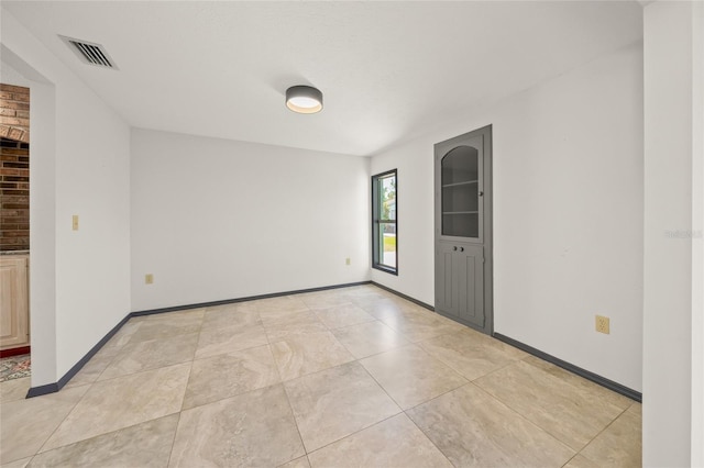 empty room featuring light tile patterned flooring, visible vents, and baseboards