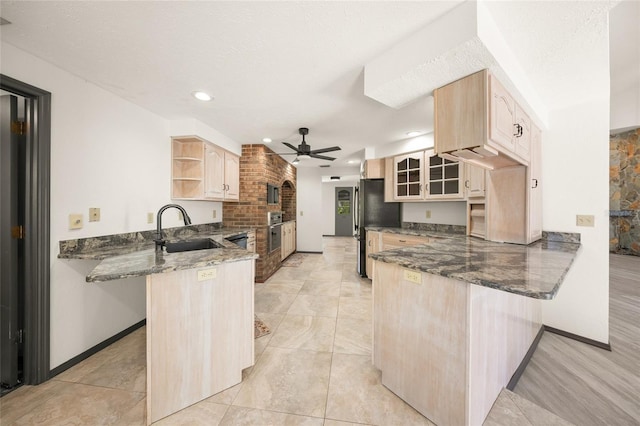 kitchen with a peninsula, open shelves, light brown cabinetry, a sink, and appliances with stainless steel finishes