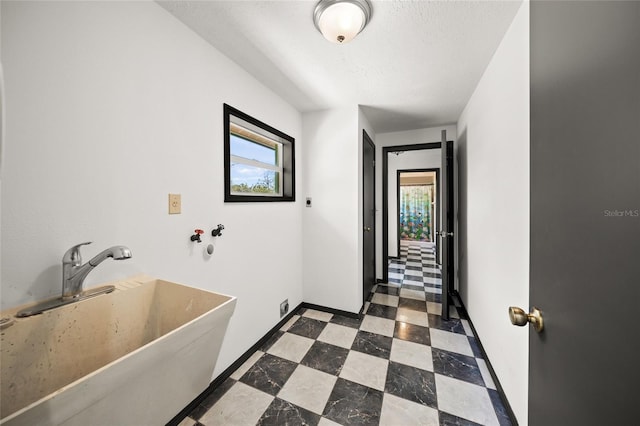 hall with a sink, baseboards, a textured ceiling, and dark floors