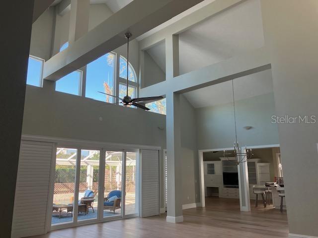 interior space featuring baseboards, high vaulted ceiling, wood finished floors, and ceiling fan with notable chandelier