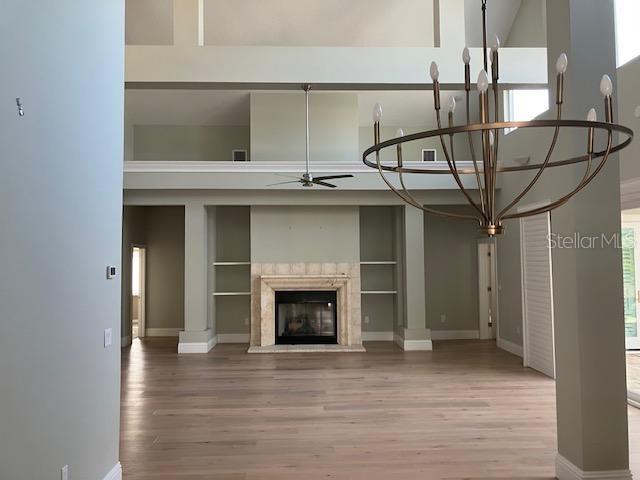 unfurnished living room with wood finished floors, a ceiling fan, a towering ceiling, and a premium fireplace