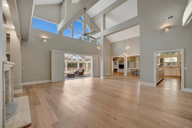 unfurnished living room featuring visible vents, baseboards, a fireplace, light wood-style floors, and ceiling fan with notable chandelier