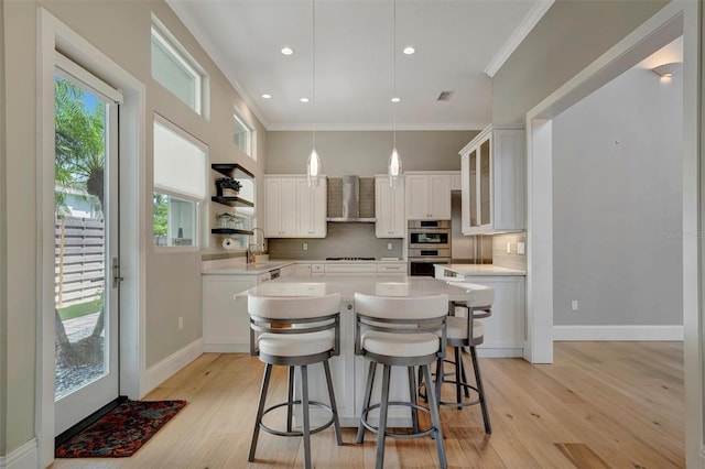 kitchen with decorative backsplash, ornamental molding, wall chimney range hood, and a kitchen island