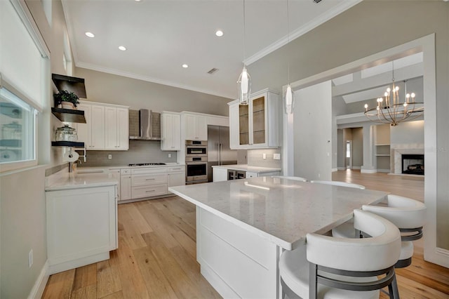 kitchen with white cabinets, crown molding, light wood finished floors, wall chimney exhaust hood, and appliances with stainless steel finishes