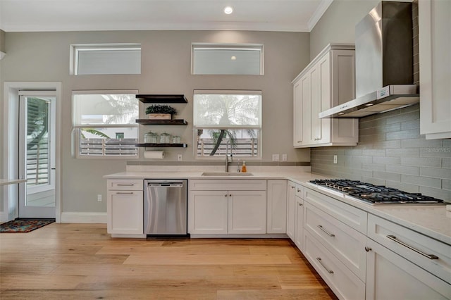 kitchen featuring light wood-style flooring, ornamental molding, stainless steel appliances, and wall chimney exhaust hood