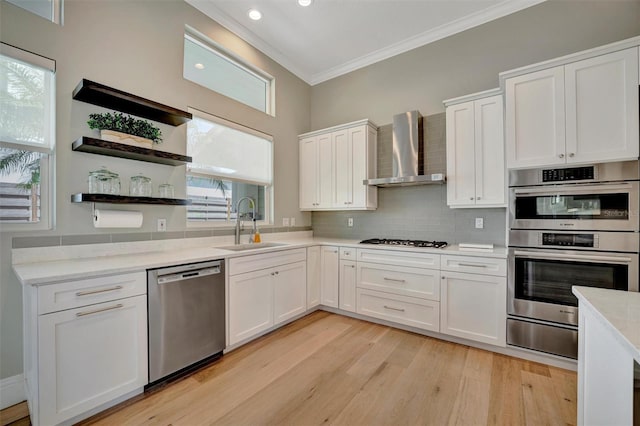 kitchen with ornamental molding, wall chimney exhaust hood, stainless steel appliances, white cabinetry, and a sink