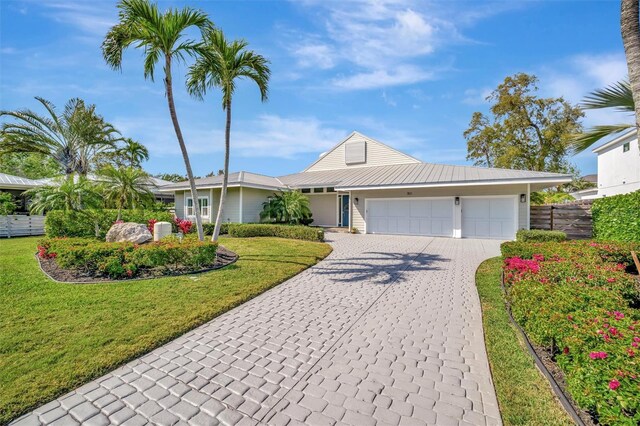 view of front of property with fence, metal roof, decorative driveway, a front lawn, and a garage
