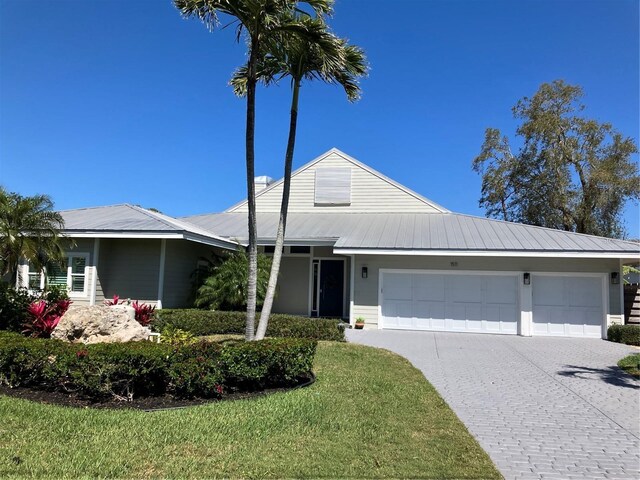 view of front of home with an attached garage, a front lawn, metal roof, and decorative driveway