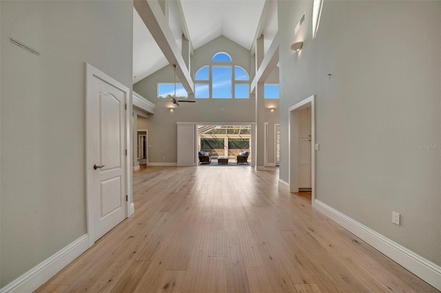 hallway with baseboards, visible vents, high vaulted ceiling, and light wood-style flooring