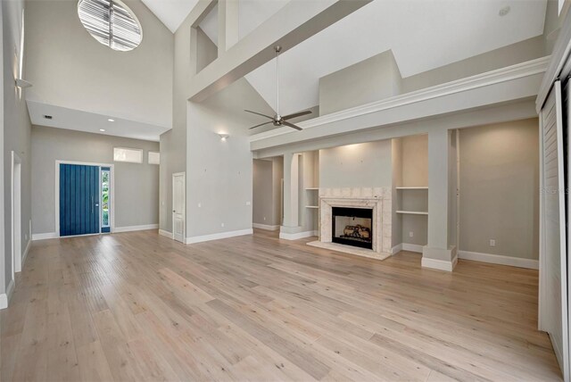 unfurnished living room with baseboards, built in shelves, light wood-style floors, ceiling fan, and a high end fireplace