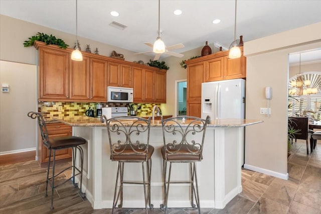 kitchen with backsplash, white appliances, a kitchen bar, and light stone countertops