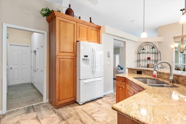 kitchen with brown cabinets, a sink, decorative light fixtures, light stone counters, and white refrigerator with ice dispenser