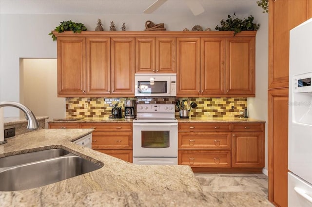 kitchen featuring white appliances, light stone counters, brown cabinets, and a sink