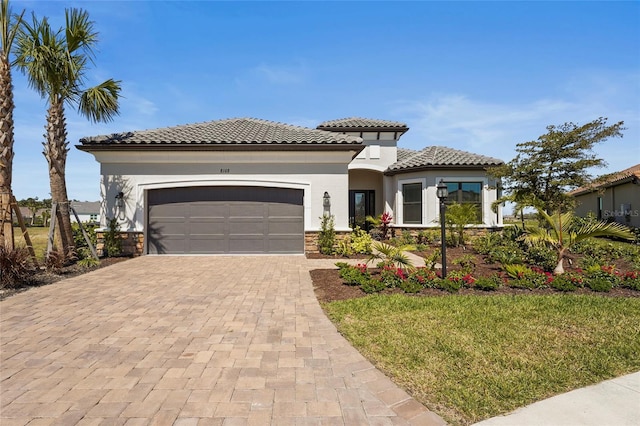 mediterranean / spanish house featuring stucco siding, a garage, stone siding, a tile roof, and decorative driveway