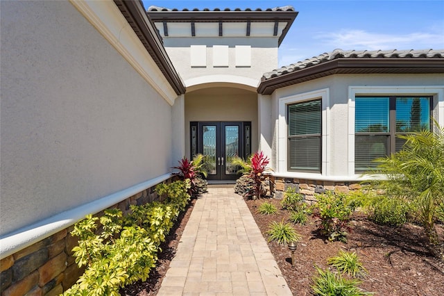 property entrance with a tiled roof, french doors, stone siding, and stucco siding