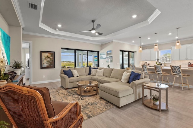 living area with visible vents, a ceiling fan, light wood-style floors, and a tray ceiling