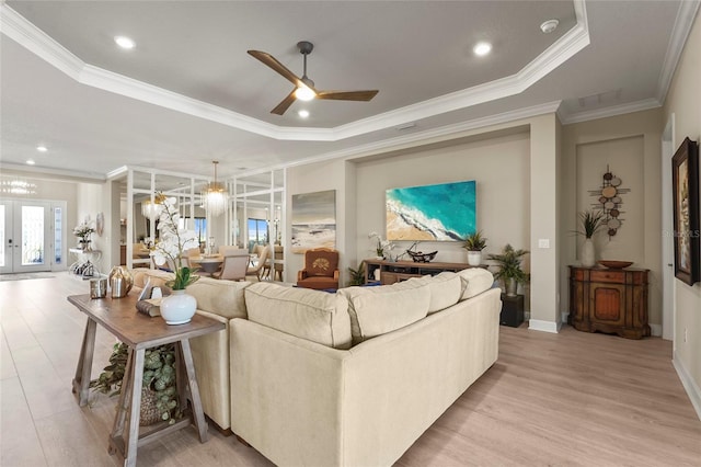 living room featuring crown molding, baseboards, light wood-type flooring, ceiling fan with notable chandelier, and a raised ceiling