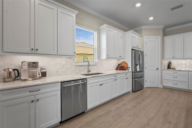 kitchen with light wood finished floors, ornamental molding, a sink, appliances with stainless steel finishes, and white cabinetry