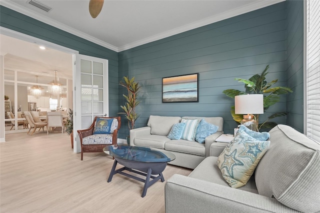 living area featuring visible vents, light wood-style flooring, ceiling fan with notable chandelier, and crown molding