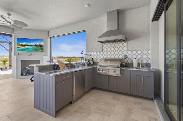 kitchen with gray cabinetry, a ceiling fan, refrigerator, a peninsula, and wall chimney range hood