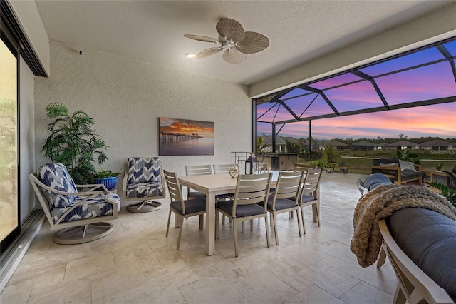 patio terrace at dusk with glass enclosure, outdoor dining area, and a ceiling fan