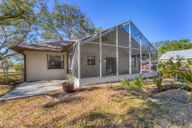 back of house with stucco siding, a lanai, and fence