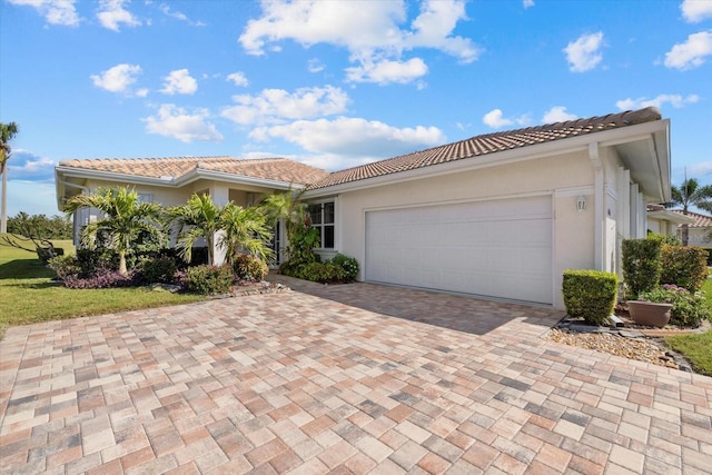 mediterranean / spanish-style home featuring stucco siding, an attached garage, a tile roof, and decorative driveway