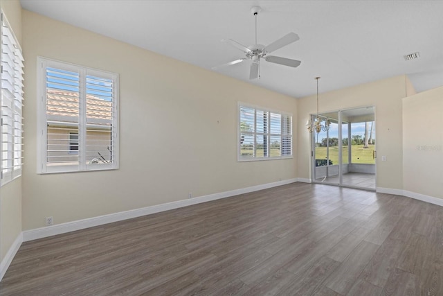 spare room featuring visible vents, ceiling fan with notable chandelier, baseboards, and wood finished floors