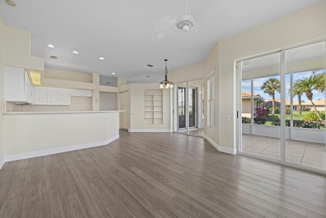 unfurnished living room with a notable chandelier, recessed lighting, baseboards, and wood finished floors