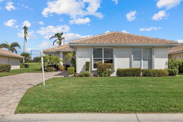 ranch-style house with a front lawn, a tiled roof, and stucco siding