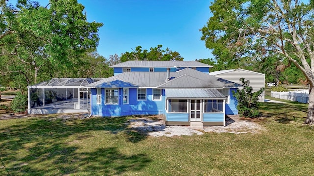 rear view of property featuring a lawn, metal roof, and glass enclosure