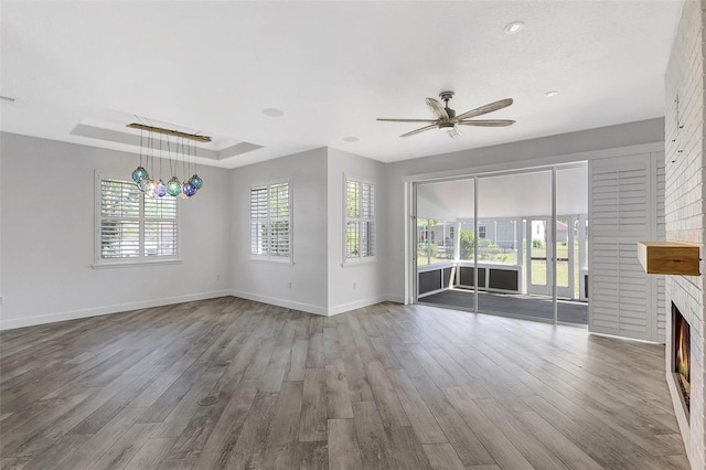 unfurnished living room featuring a tray ceiling, wood finished floors, a fireplace, and baseboards