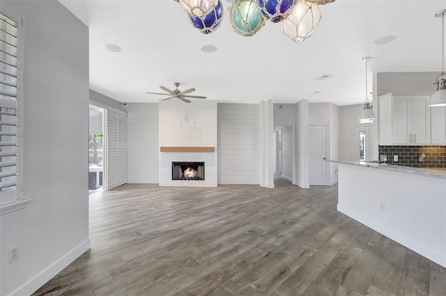 unfurnished living room with ceiling fan, a brick fireplace, wood finished floors, and a healthy amount of sunlight