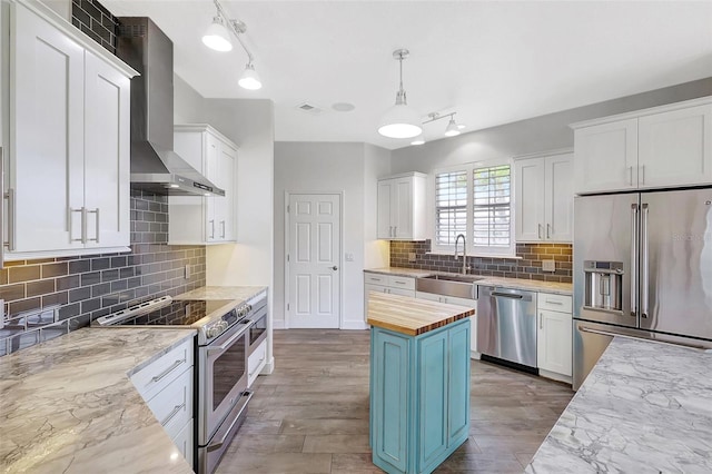 kitchen with wall chimney range hood, butcher block countertops, stainless steel appliances, white cabinetry, and a sink