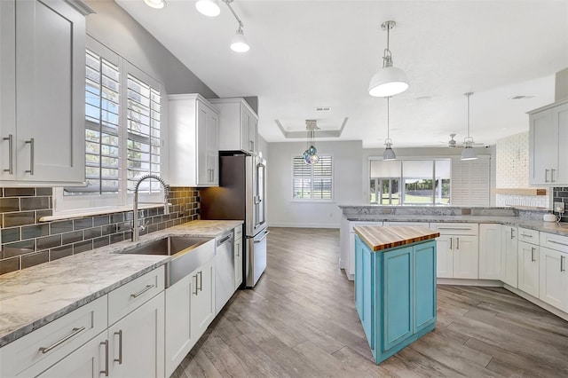 kitchen with blue cabinetry, butcher block counters, light wood-type flooring, stainless steel appliances, and a sink