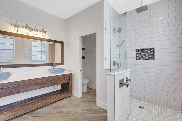 bathroom featuring toilet, walk in shower, wood finished floors, and a sink