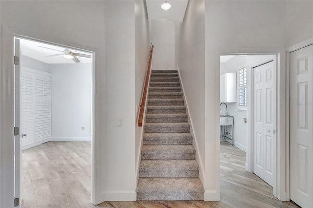 staircase with a ceiling fan, baseboards, and wood finished floors