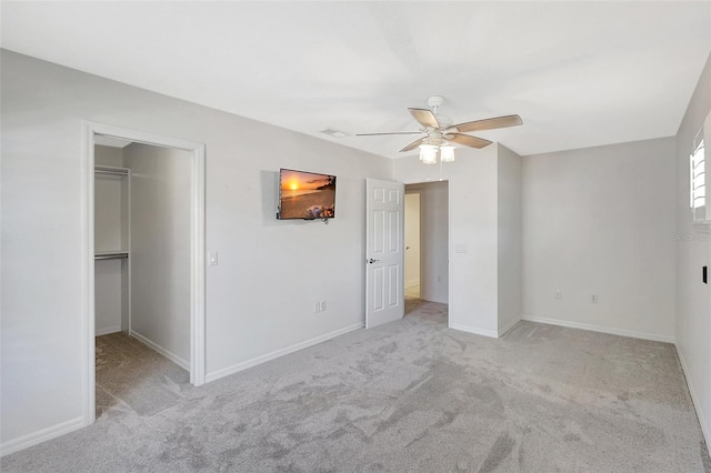 unfurnished bedroom featuring a walk in closet, baseboards, carpet floors, and ceiling fan