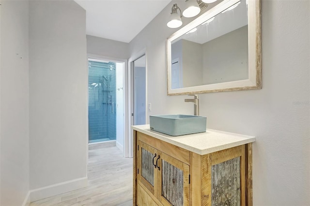 full bath featuring baseboards, wood finished floors, vanity, and a tile shower