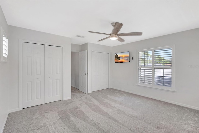 unfurnished bedroom featuring visible vents, multiple closets, a ceiling fan, carpet, and baseboards