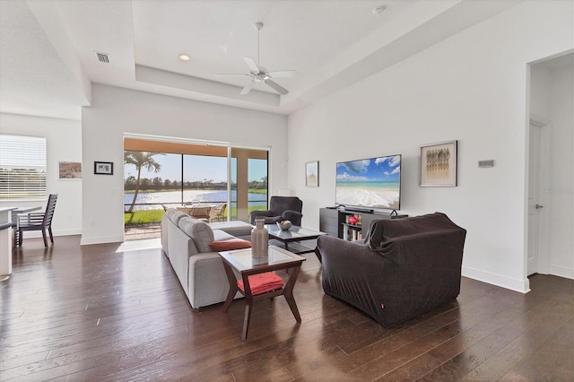 living area featuring a raised ceiling, visible vents, dark wood-style flooring, and baseboards