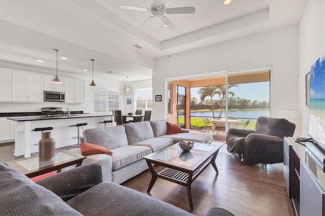 living area featuring dark wood-style floors, a tray ceiling, a high ceiling, recessed lighting, and ceiling fan with notable chandelier