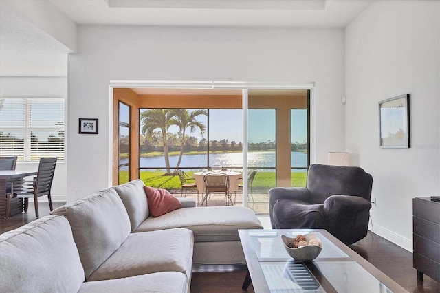 living area featuring dark wood finished floors, a raised ceiling, baseboards, and a water view