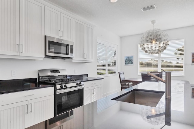 kitchen featuring visible vents, a notable chandelier, dark countertops, appliances with stainless steel finishes, and white cabinets