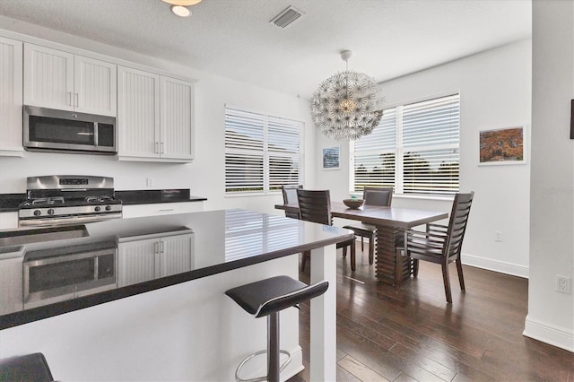 kitchen featuring dark countertops, visible vents, dark wood-type flooring, appliances with stainless steel finishes, and hanging light fixtures