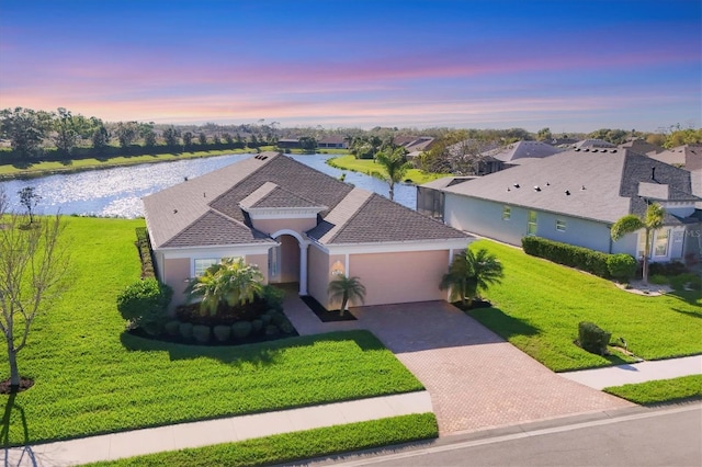 view of front facade with a water view, a residential view, decorative driveway, a yard, and a garage